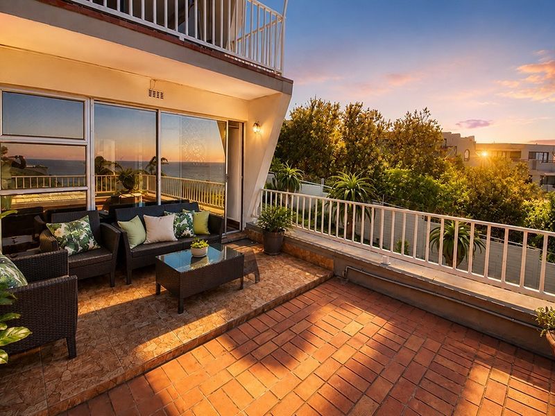 Spacious outdoor balcony featuring tiled flooring, a secure metal balustrade, and large sliding glass doors providing seamless indoor-outdoor flow with sunset views.