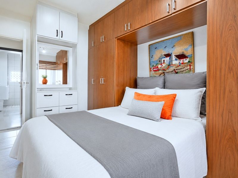 A well-maintained bedroom featuring extensive built-in wooden cabinetry, overhead storage, and a dedicated vanity area with integrated lighting.