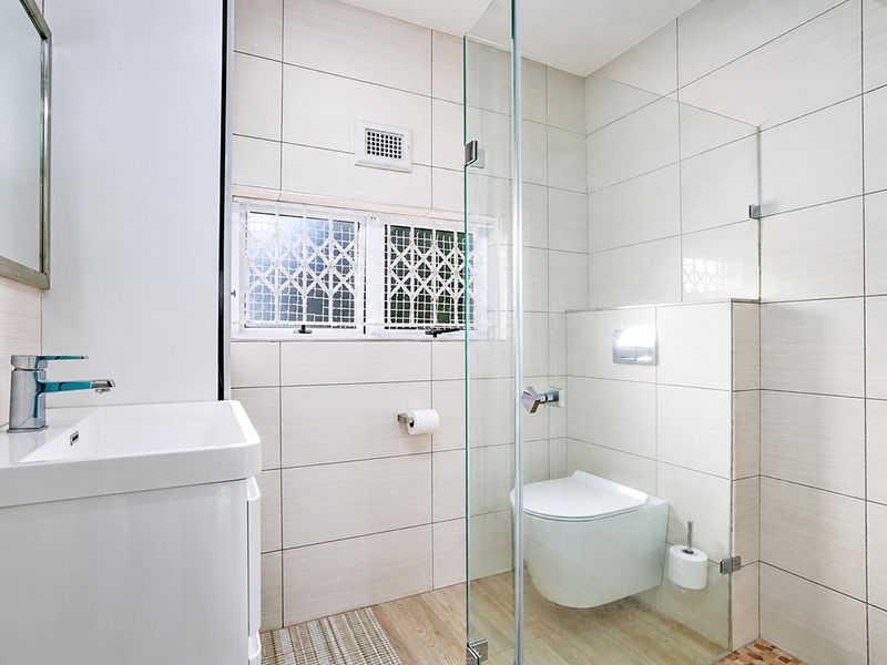 Modern bathroom featuring a wall-mounted toilet, glass shower enclosure, vanity basin with chrome fixtures, and neutral wall tiling.