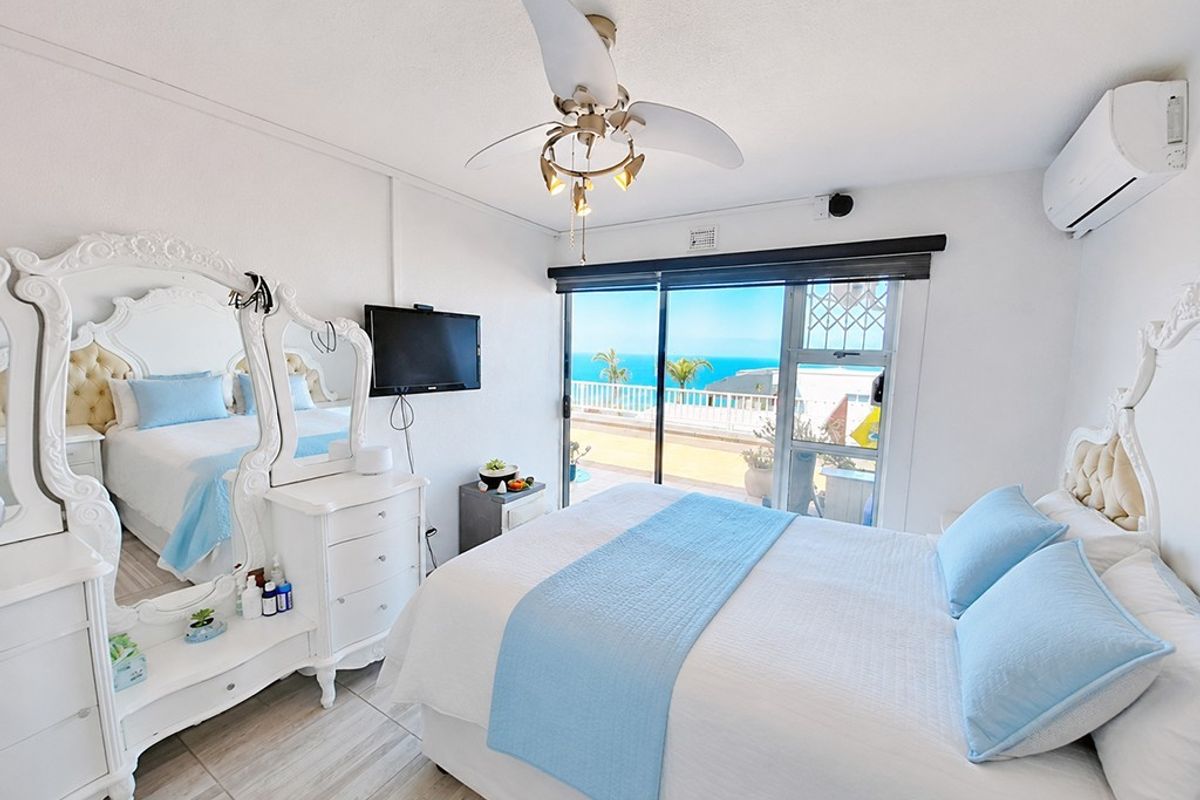 Bright bedroom featuring a ceiling fan, split-system air conditioning, and sliding glass doors that open to a balcony with ocean views.