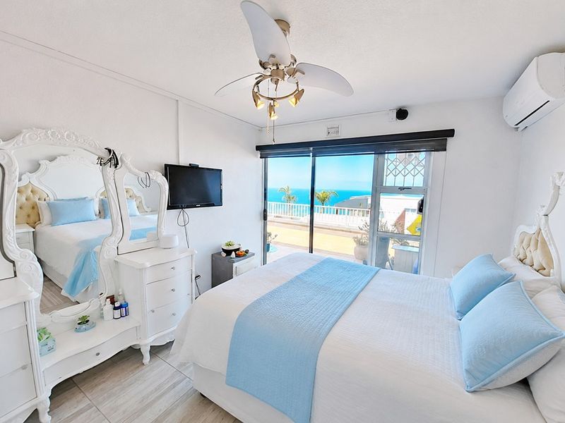 Bright bedroom featuring a ceiling fan, split-system air conditioning, and sliding glass doors that open to a balcony with ocean views.