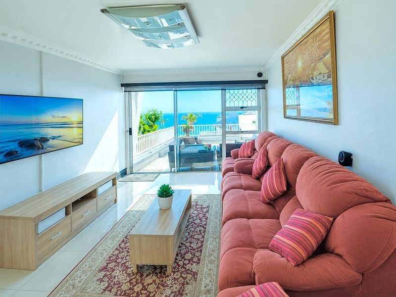 Bright living room featuring tiled floors, decorative ceiling cornices, and large sliding glass doors opening onto a balcony with ocean views.
