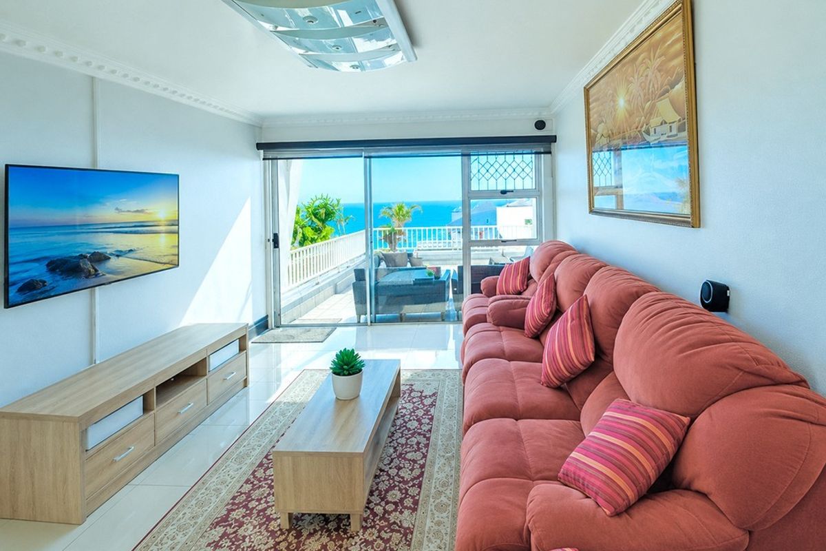 Bright living room featuring tiled floors, decorative ceiling cornices, and large sliding glass doors opening onto a balcony with ocean views.