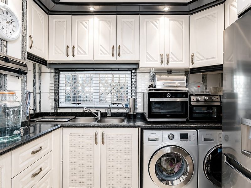 A compact, well-organized kitchen featuring granite countertops, white cabinetry, a double basin sink, and integrated laundry appliances.