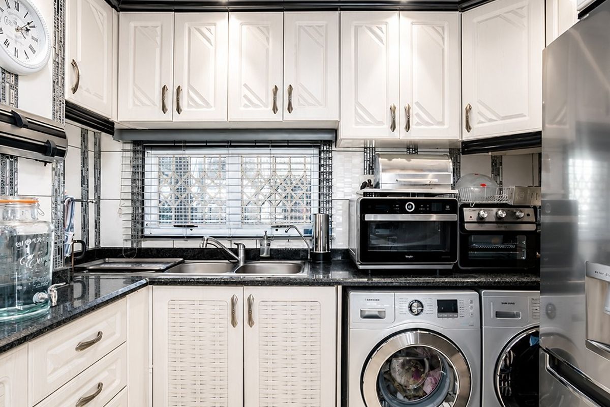 A compact, well-organized kitchen featuring granite countertops, white cabinetry, a double basin sink, and integrated laundry appliances.