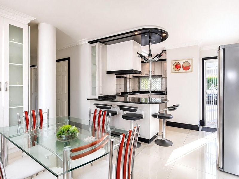 Modern open-plan kitchen and dining area featuring a breakfast bar, granite countertops, sleek cabinetry, and polished tiled flooring with direct access to the exterior.