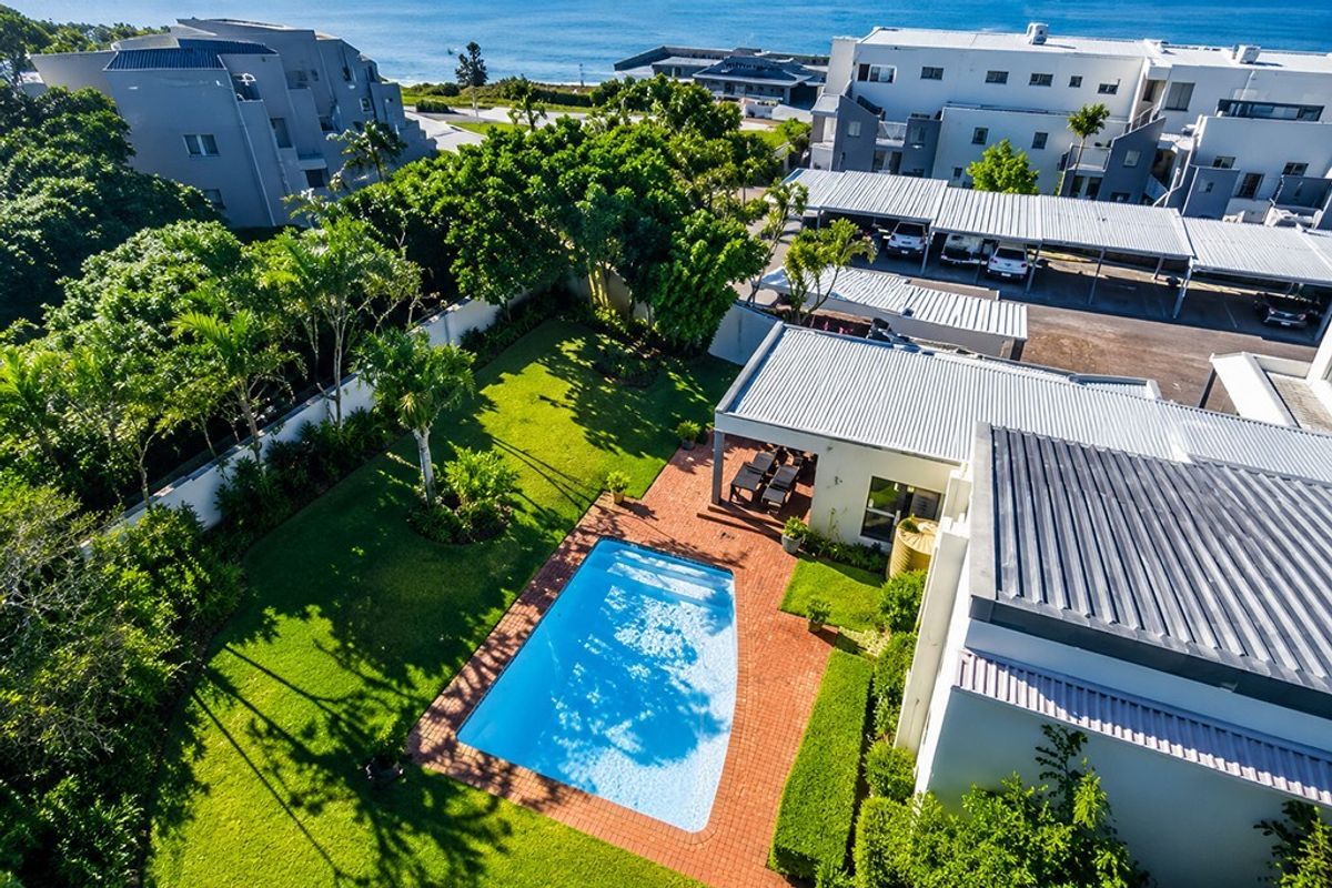 Aerial view of the apartment complex featuring a private swimming pool, covered patio, landscaped garden, and dedicated carport parking area.