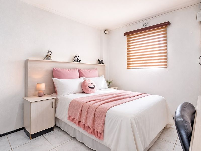 A well-maintained bedroom featuring tiled flooring, a built-in headboard, and a roller blind for privacy.