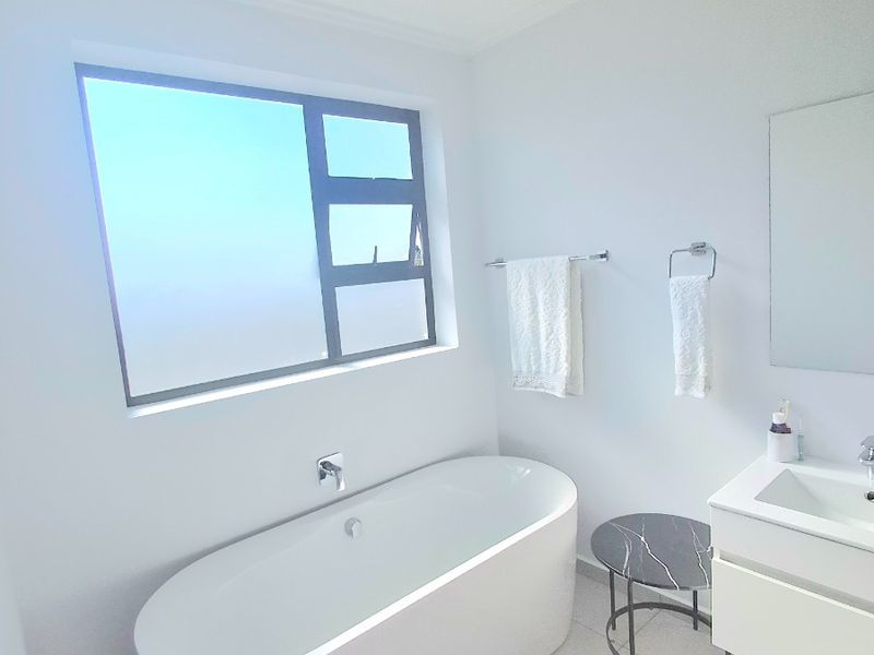 Modern bathroom featuring a sleek freestanding bathtub, wall-mounted mixer, and a contemporary vanity unit with an integrated basin.