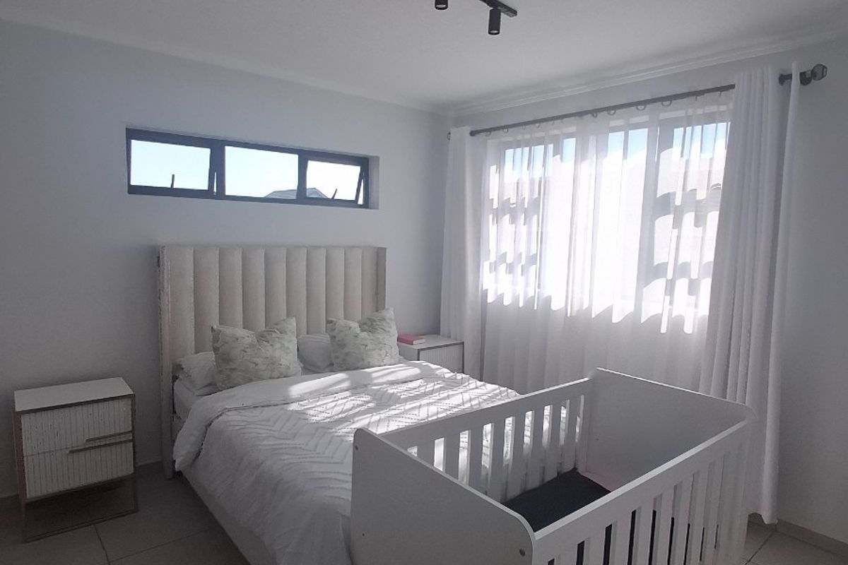 A bright, modern bedroom featuring neutral tiled flooring, contemporary track lighting, and a combination of large windows and a clerestory window for natural light.
