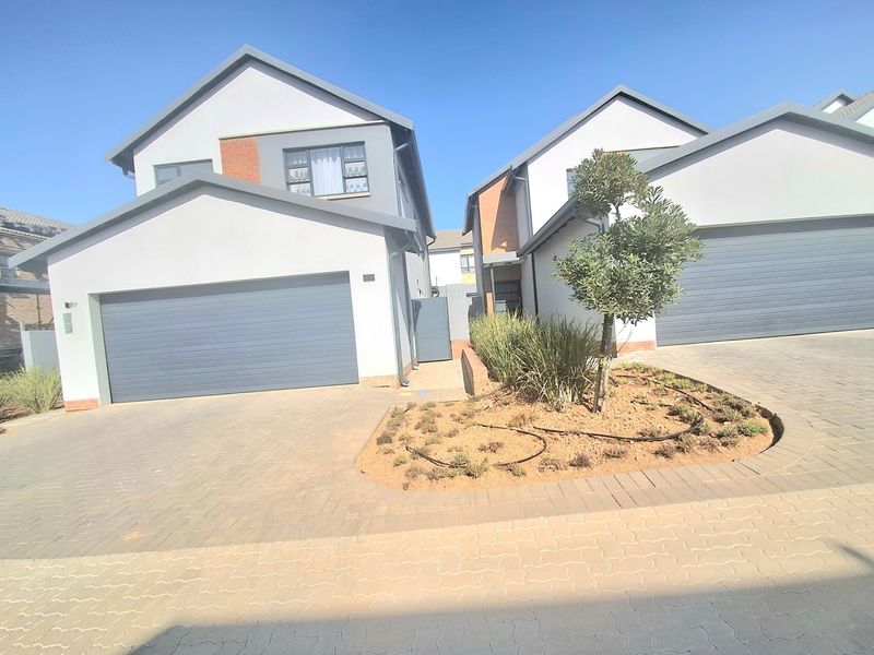 Front view of a modern double-story residential property featuring a paved driveway, double garage, and a landscaped garden bed.