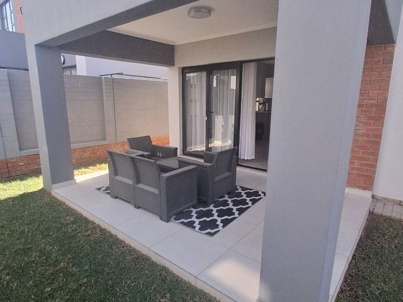 A covered patio area featuring tiled flooring and sliding glass door access to the interior living space, overlooking a private garden.