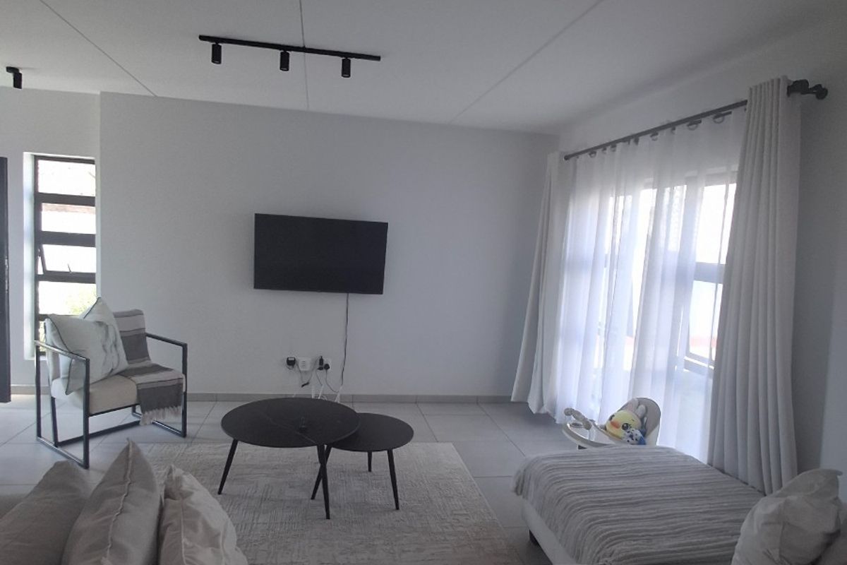 A bright and spacious living room featuring neutral tiled flooring, modern track lighting, and large windows that allow for ample natural light.