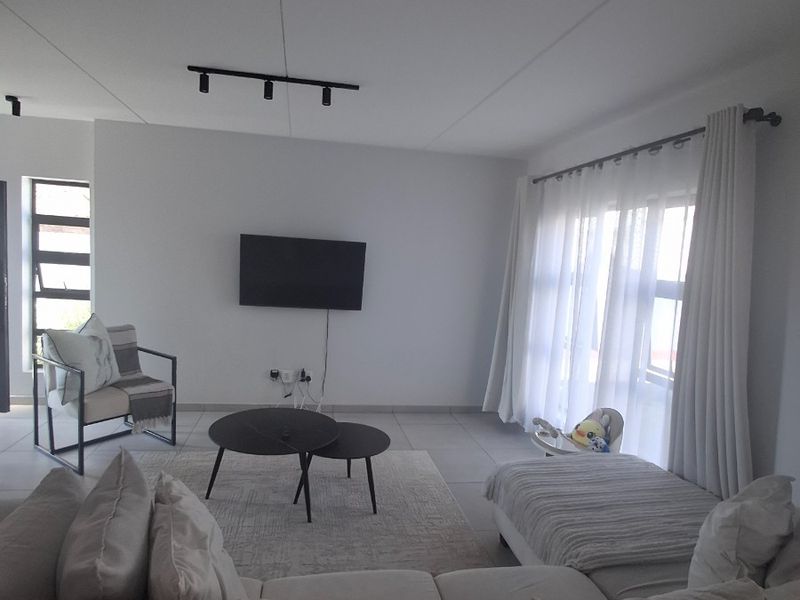 A bright and spacious living room featuring neutral tiled flooring, modern track lighting, and large windows that allow for ample natural light.