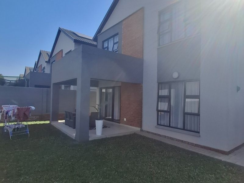 Rear view of a modern double-storey house featuring a covered patio, lawn area, and contemporary brick and plaster facade.