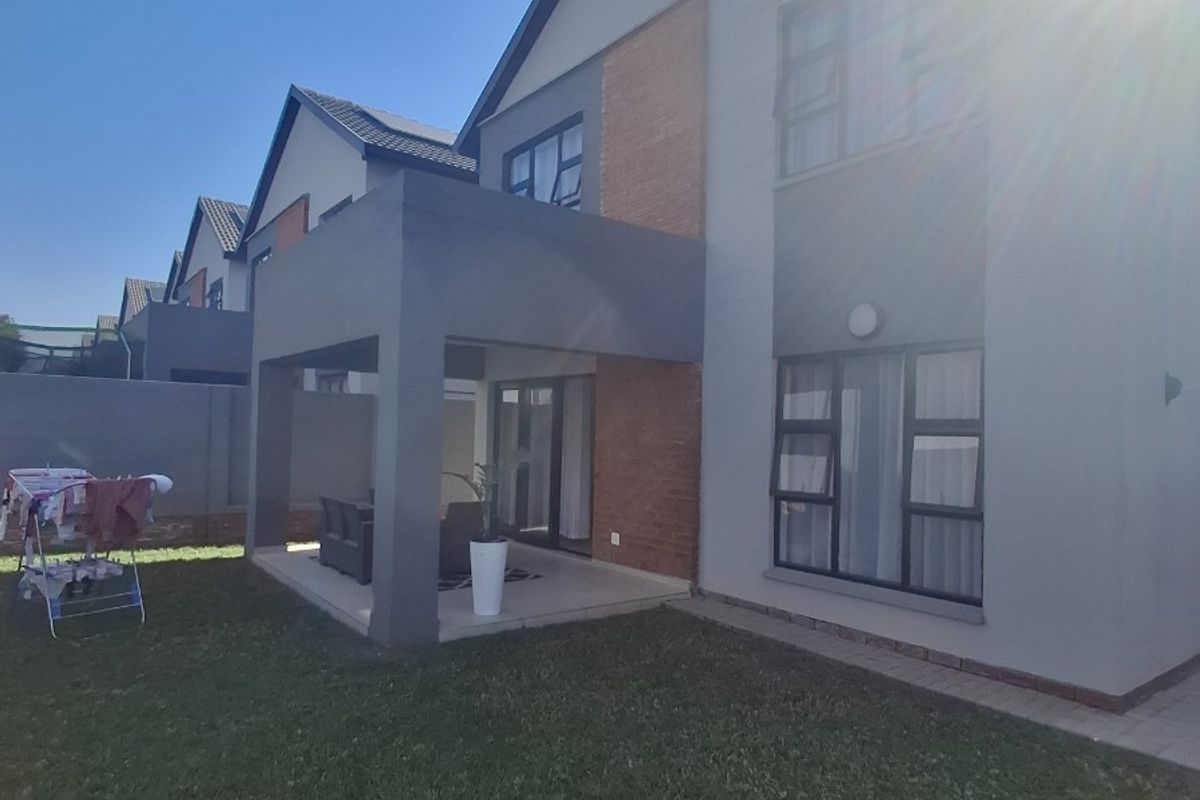 Rear view of a modern double-storey house featuring a covered patio, lawn area, and contemporary brick and plaster facade.