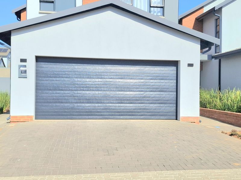 A modern residential garage featuring a dark sectional door and a clean paved driveway, set against a contemporary building facade.