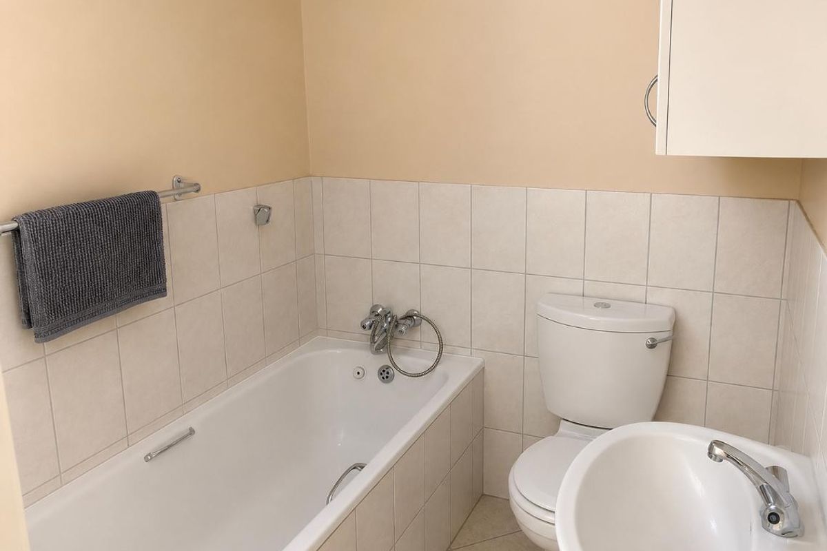 A functional bathroom featuring a standard bathtub, toilet, and pedestal basin with neutral wall tiling and a wall-mounted storage cabinet.