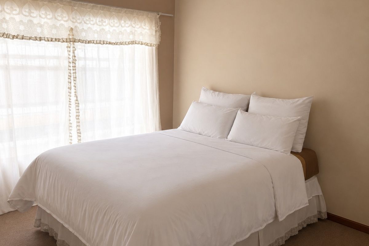 A neutrally painted bedroom featuring carpeted flooring and a large window with installed curtain hardware.
