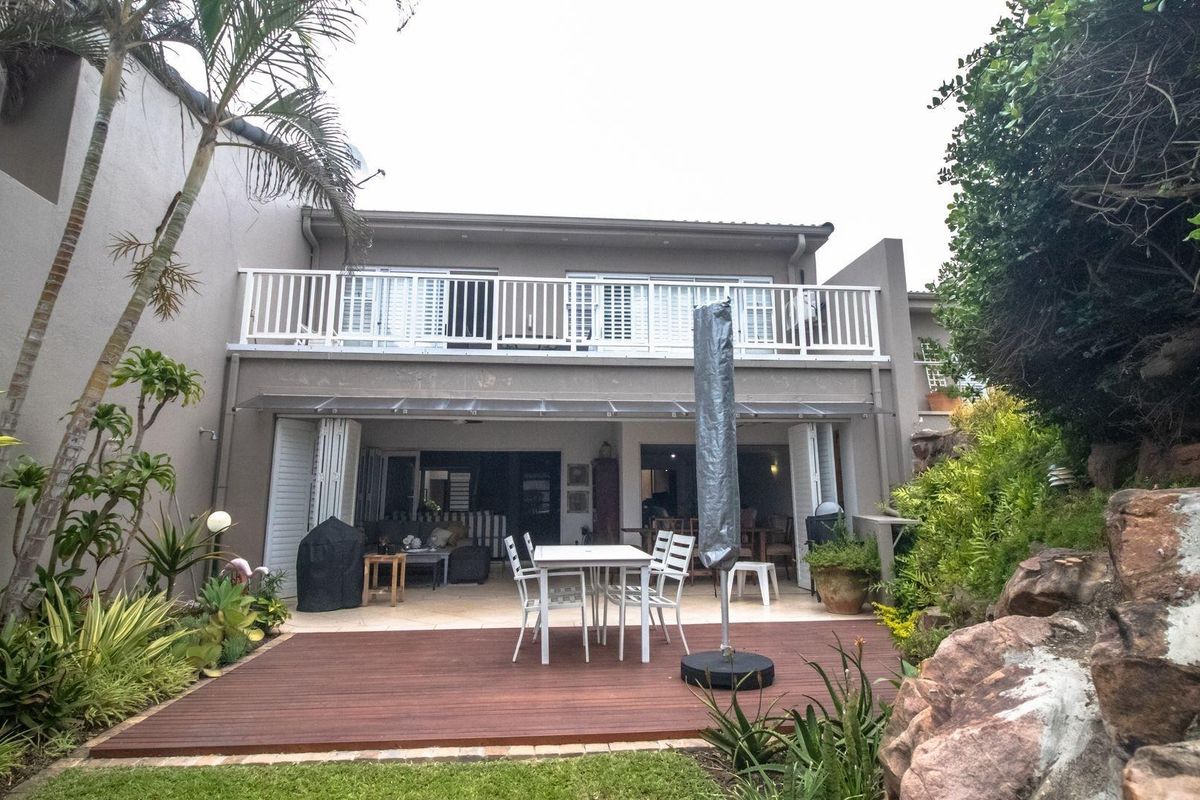 Rear view of the townhouse featuring a timber deck, landscaped garden, and an upper-level balcony with white balustrades and bi-fold doors.
