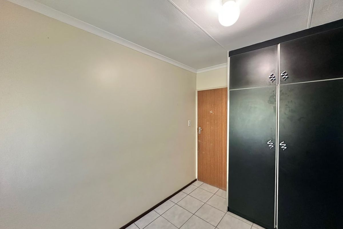 A clean, empty bedroom featuring tiled flooring, a coved ceiling, and built-in black cupboards.