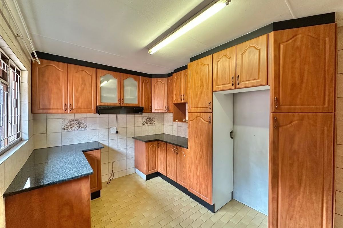 A functional kitchen featuring wood-look laminate cabinetry, granite countertops, tiled backsplash, and an integrated extractor fan, offering a clean and practical workspace.