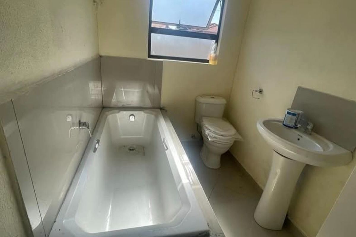 A functional bathroom featuring a standard bathtub, pedestal basin, and toilet with tiled splashbacks and flooring.