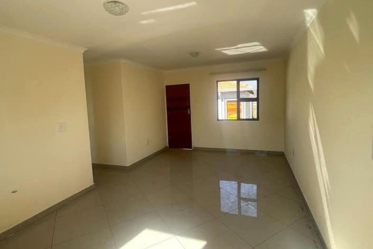 A bright, empty living area featuring neutral walls, tiled flooring, and a window providing natural light.