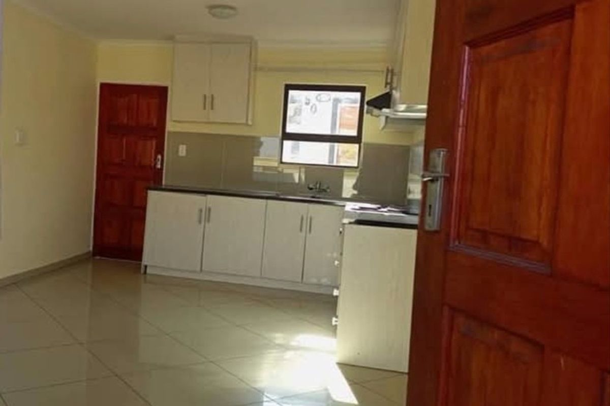 An open-plan kitchen featuring white built-in cabinetry, tiled flooring, and a functional layout, viewed from an adjacent doorway.