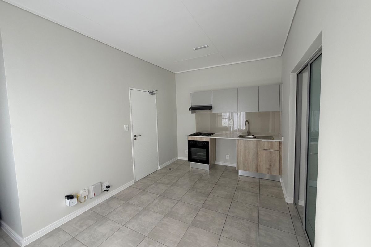 Modern open-plan kitchen and living area featuring neutral cabinetry, built-in appliances, tiled flooring, and access to an outdoor space via sliding glass doors.
