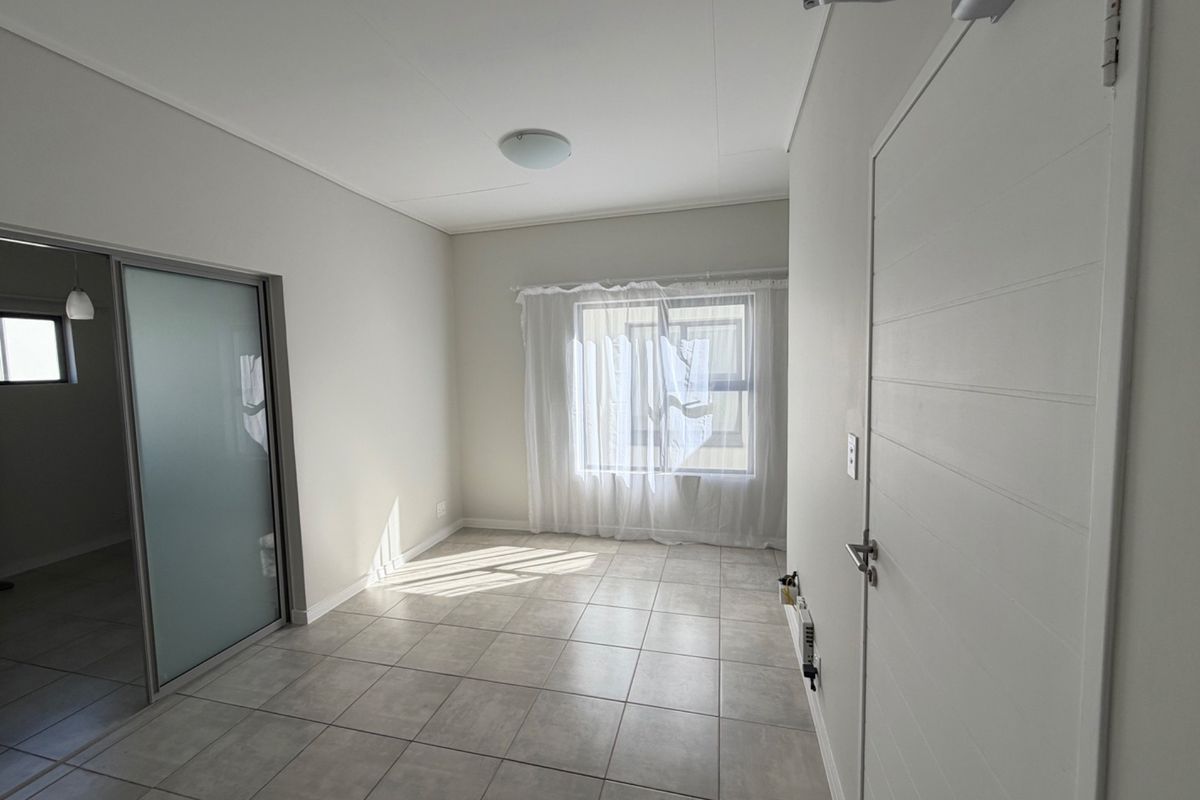 A bright, empty bedroom featuring neutral tiled flooring, a sliding door, and a clean, modern finish throughout.