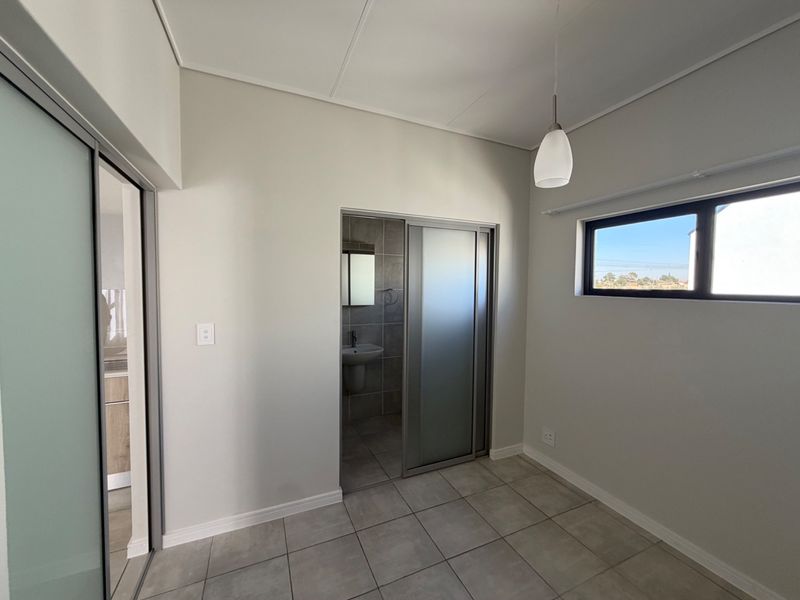 A clean, modern bedroom featuring neutral tiled flooring, a sliding door leading to an en-suite bathroom, and a horizontal window providing natural light.