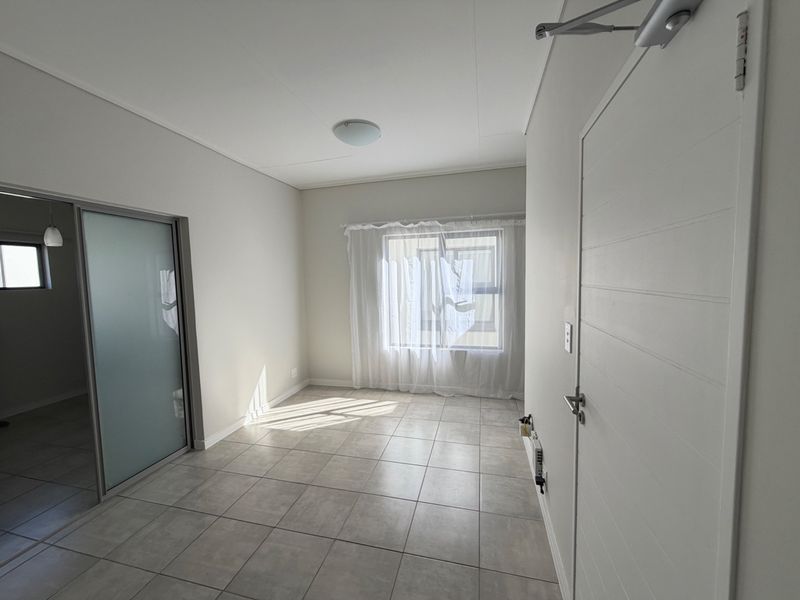 A bright, empty bedroom featuring neutral tiled flooring, a sliding door, and a clean, modern finish throughout.