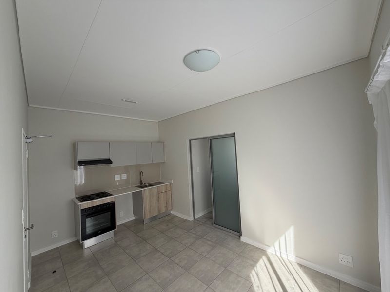 A clean, modern open-plan kitchen featuring built-in cabinetry, an oven, hob, extractor fan, and tiled flooring, presented in a vacant, well-maintained condition.
