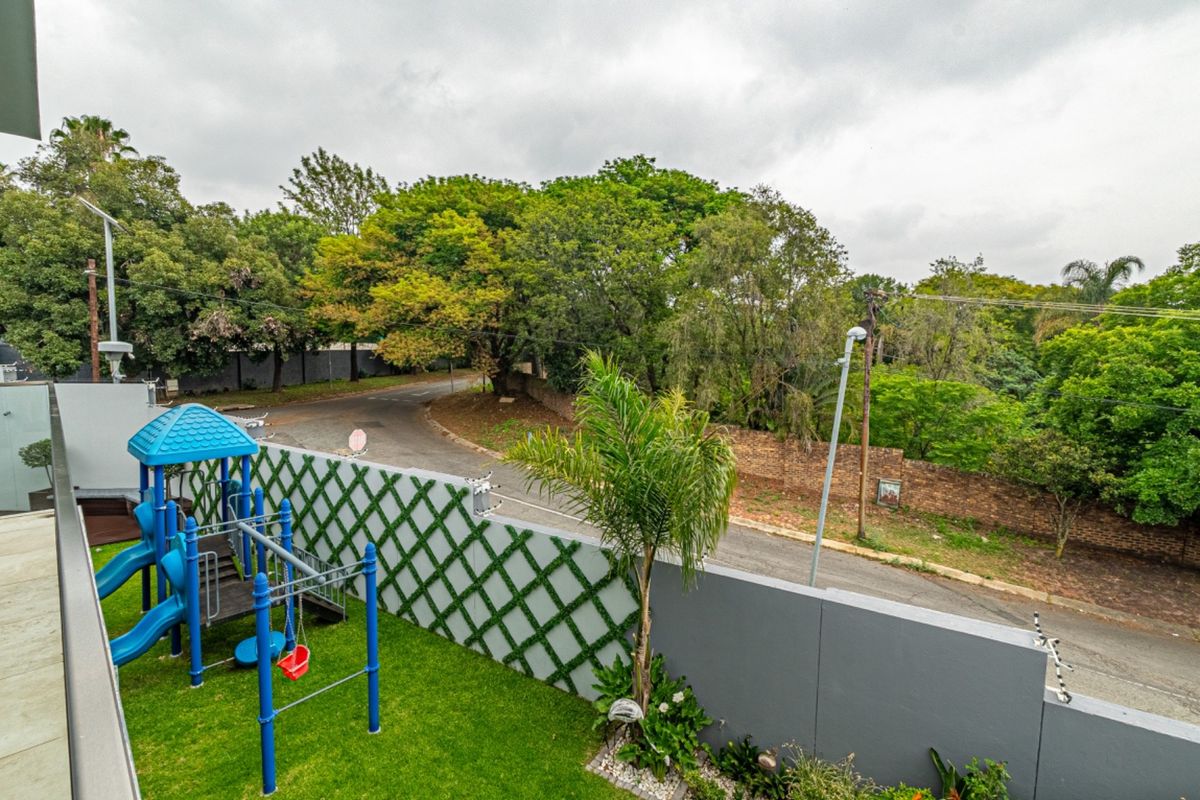 A view of the rear garden area featuring a well-maintained lawn, perimeter wall with electric fencing, and a view of the adjacent street.