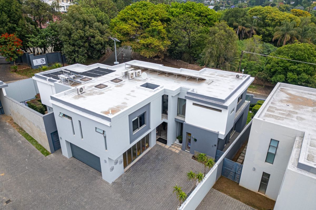 Aerial view of a modern two-story residential property featuring a paved driveway, double garage, and rooftop solar infrastructure set within a landscaped estate.
