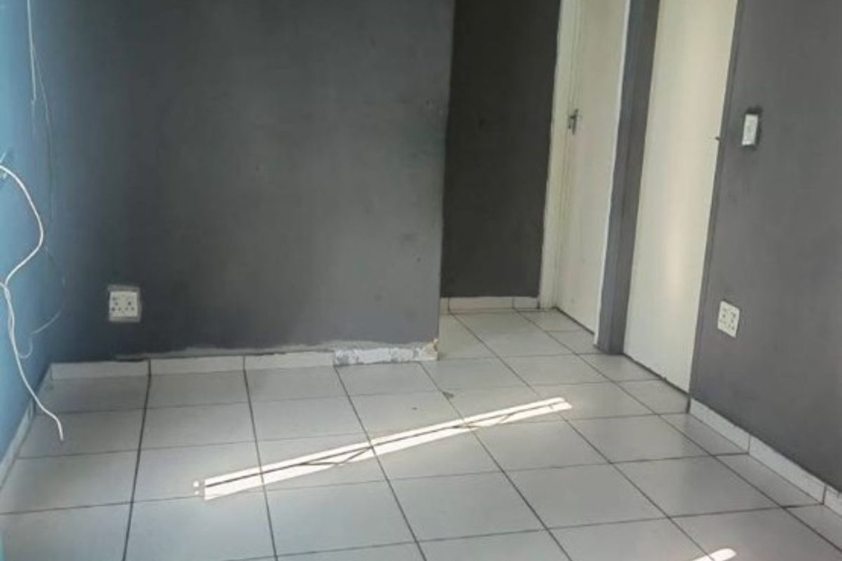 An empty living area featuring tiled flooring and dark grey walls, requiring minor cosmetic repairs and fresh paint to enhance its appeal.