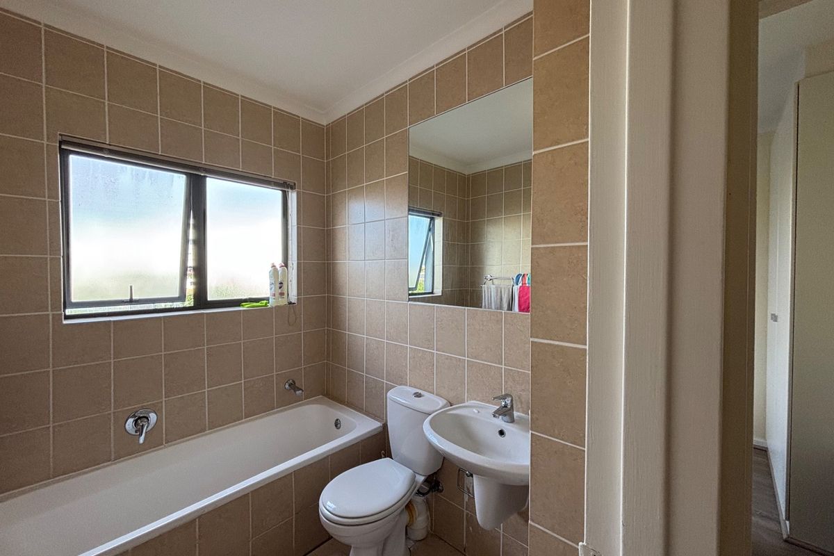 A functional bathroom featuring neutral wall tiles, a bathtub, a pedestal basin, and a wall-mounted mirror, offering a clean and practical layout.
