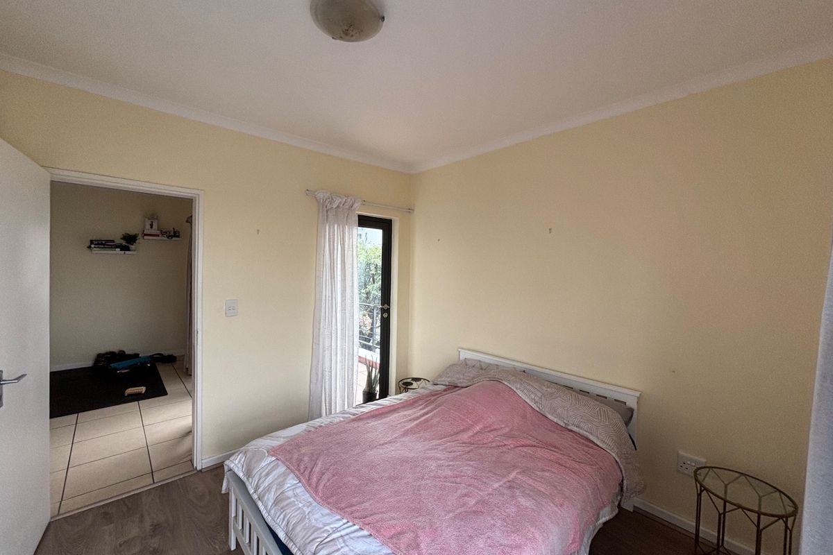 A bedroom featuring laminate flooring, a glass door leading to a balcony, and neutral wall finishes.