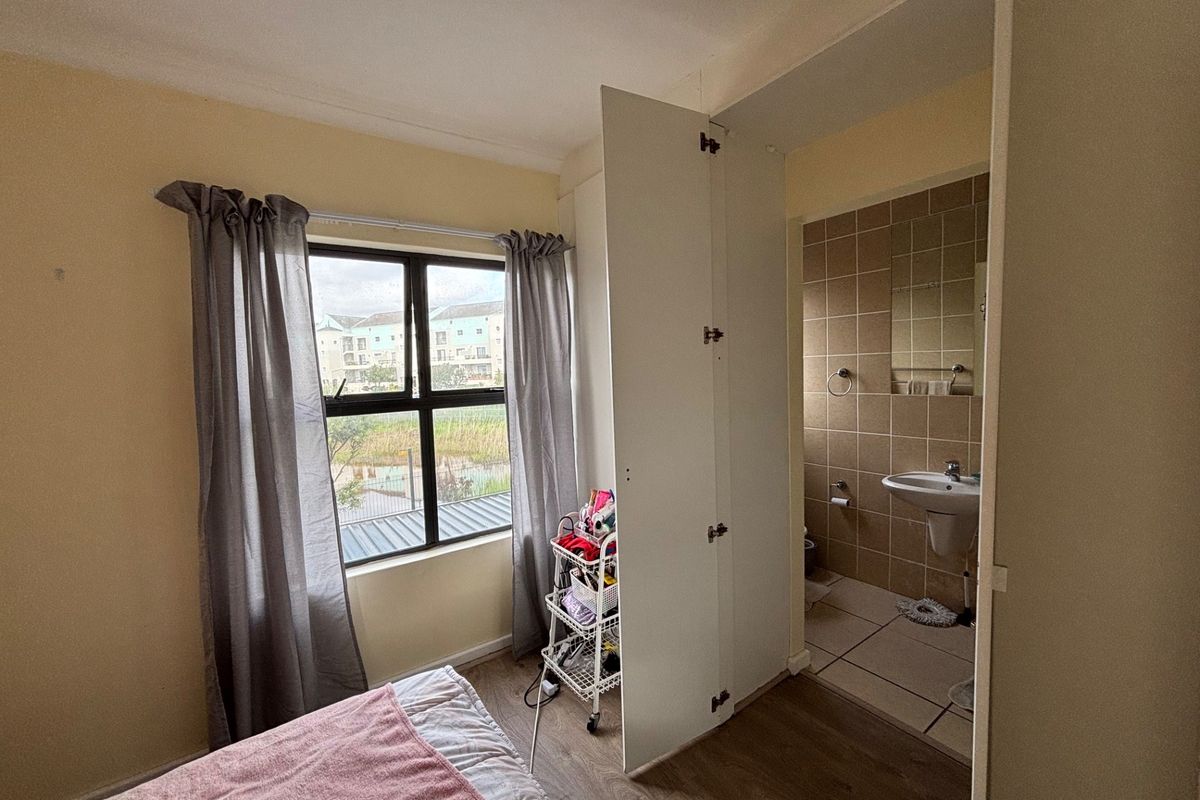 Bedroom featuring laminate flooring, a built-in cupboard, and an adjoining en-suite bathroom with tiled finishes and a pedestal basin.