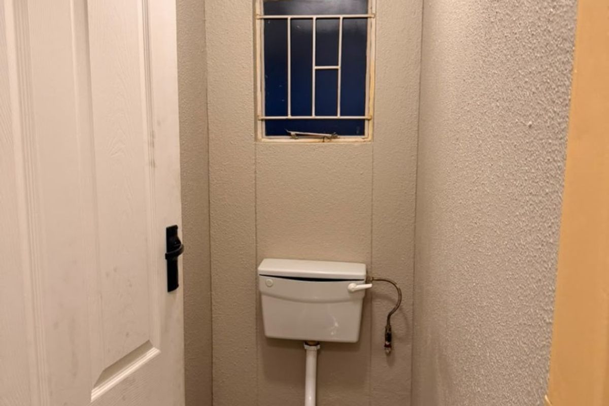 A compact, functional guest toilet featuring tiled floors and a small window with security bars.