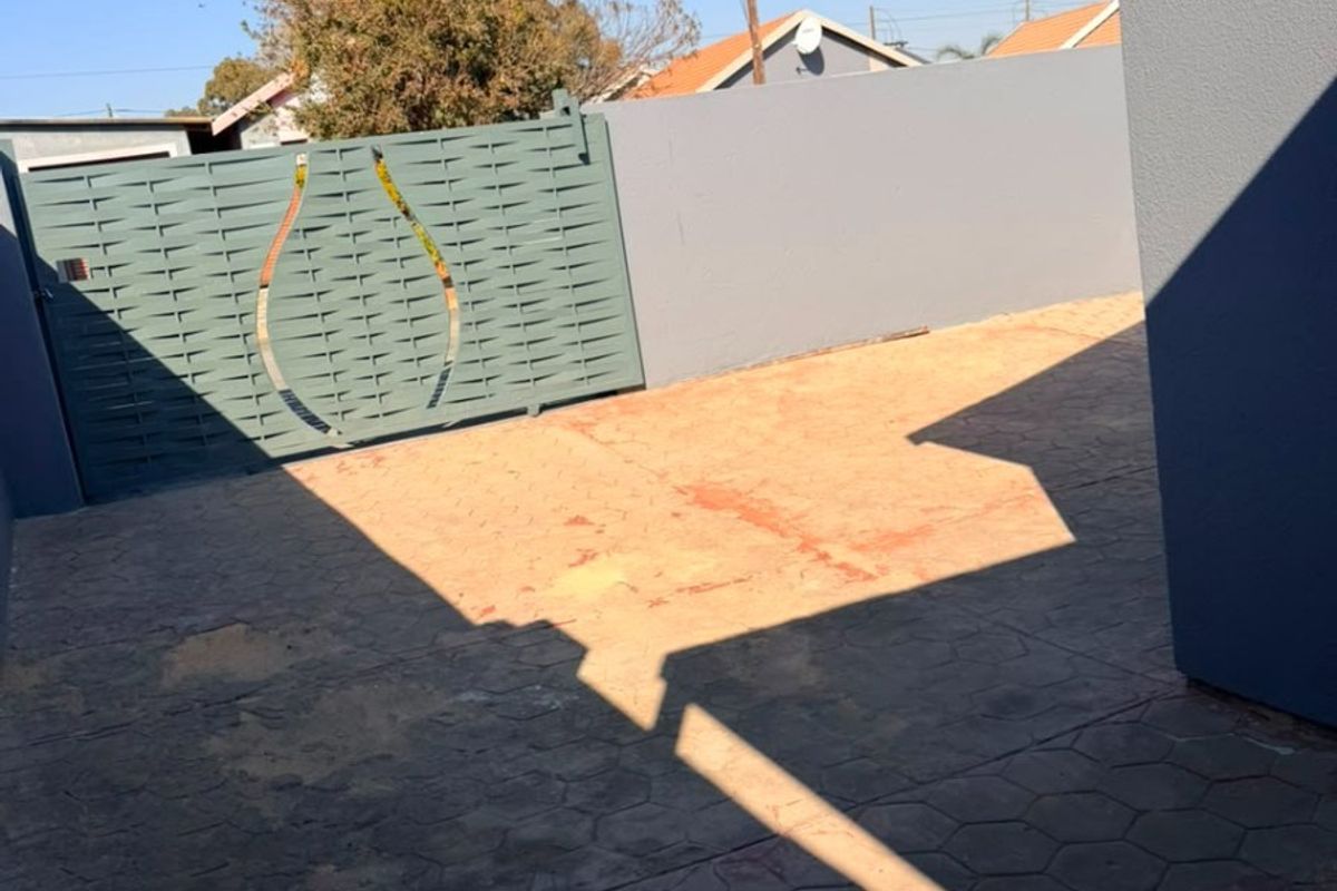 A private rear courtyard featuring paved flooring, a solid boundary wall, and a decorative metal gate.