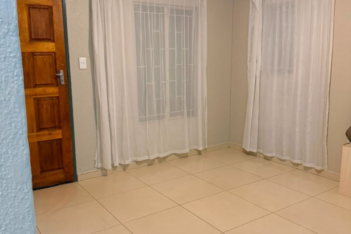 A clean, empty bedroom featuring neutral tiled flooring, security bars on the windows, and a solid wooden door.