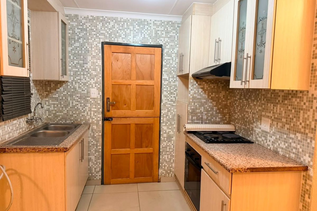 A functional kitchen featuring light wood cabinetry, granite countertops, a mosaic tile backsplash, and integrated cooking appliances.