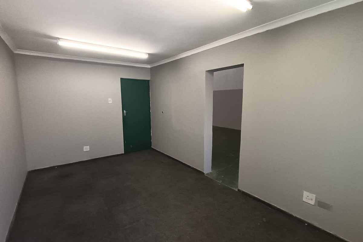 An empty, neutral-toned utility or office space featuring fluorescent lighting, coved ceilings, and direct access to an adjoining room.