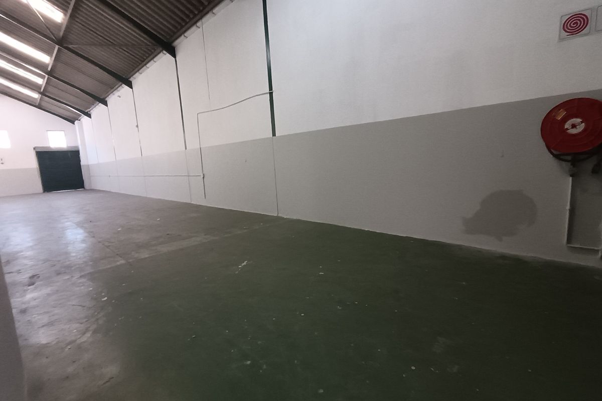 Spacious industrial warehouse unit featuring high ceilings with exposed steel trusses, skylights, painted concrete flooring, and a wall-mounted fire hose reel.