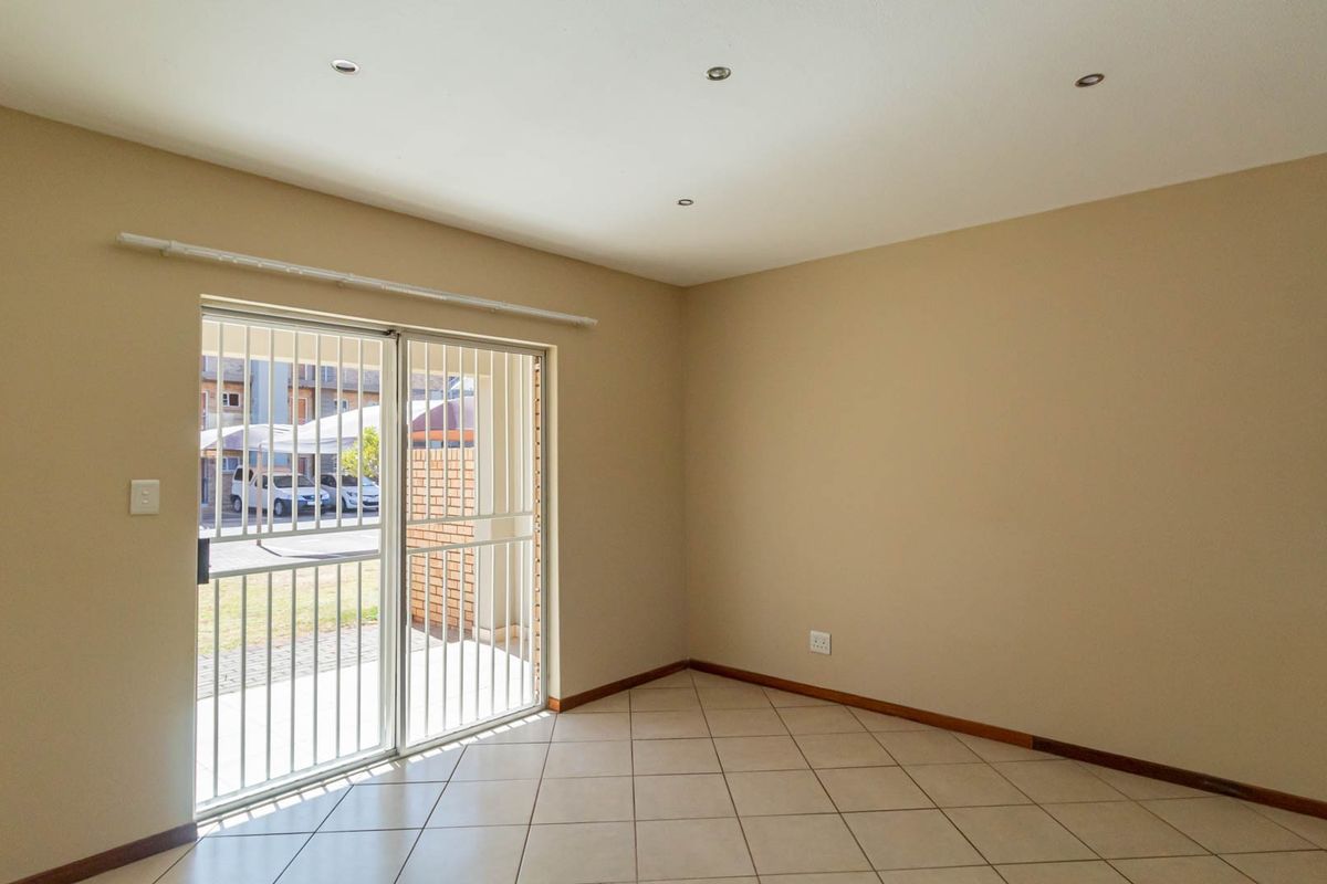 An empty, well-lit living area featuring neutral tiled flooring, recessed ceiling lights, and a sliding glass door with an integrated security gate.