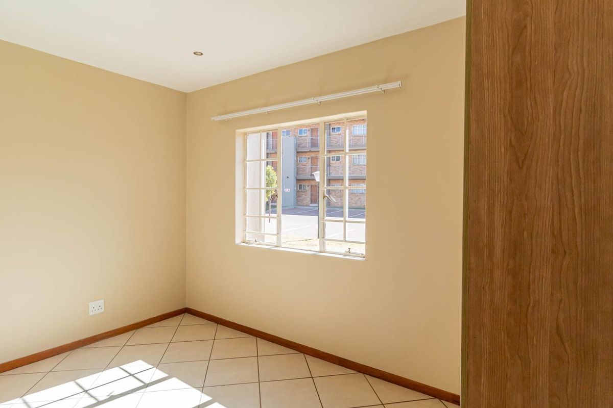An empty bedroom featuring neutral wall paint, tiled flooring, and a built-in cupboard, offering a clean canvas for personalization.