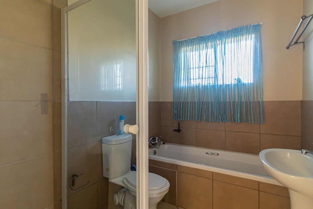 A functional bathroom featuring a shower enclosure, bathtub, pedestal basin, and neutral wall tiling.