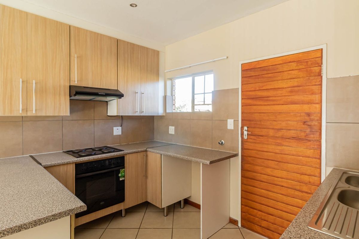A functional kitchen featuring light wood-look cabinetry, granite-style countertops, built-in oven and hob, and a double stainless steel sink with tiled splashbacks.